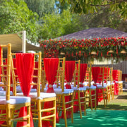 Decorated outdoor event with red chairs and tables under a floral canopy. Moments Rentals