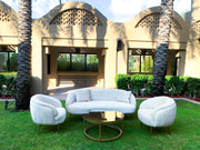outdoor sofa set with two chairs on a grassy area in front of a building with palm trees.