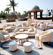 Outdoor seating area with beige sofas, armchairs, and ottomans on a sunny day.