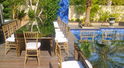Outdoor dining setup by a pool with chairs and table on a wooden deck. Moments rentals