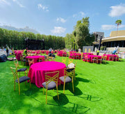 Outdoor event setup with pink tables and chairs on a grassy area. moments rentals