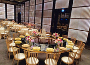 Decorated event space with round tables and chairs, floral arrangements, and a large screen.