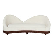 A modern curved daybed with a beige upholstered seat and sculptural backrest, supported by a dark brown fluted base with small turned wooden legs.