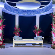 Decorative canopy with floral arrangements and a bridal bench underneath at night.