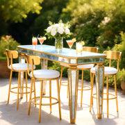 Outdoor table set with glasses of cocktails and flowers, surrounded by chairs on a sunny day.