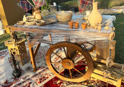 Wooden table with decorative items including vases and a large wooden wheel on a patterned rug outdoors.