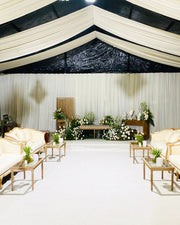 Decorated event space with floral arrangements, chairs, and tables under a black and white tent.