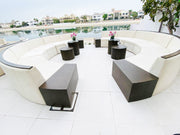 Modern outdoor seating area with white curved sofa and black tables by a poolside.