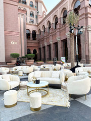 Luxurious outdoor seating area with white sofas and gold coffee tables in front of a grand building.