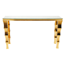 A cocktail table with a clear glass top and highly reflective, wavy gold metal legs, shown against a plain white background.
