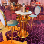 Gold bar table with stools on a purple patterned carpet in a formal event setting.