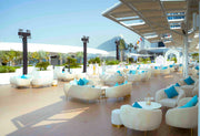 Outdoor seating area with white chairs and blue cushions on a deck with a view of futuristic architecture.