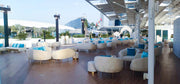 Outdoor seating area with white chairs and blue cushions on a wooden deck, with a cityscape in the background.