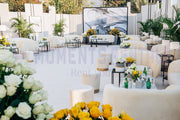Decorative outdoor setting with white furniture, flowers, and a large screen displaying an abstract art piece.