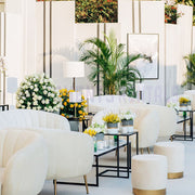 Modern indoor event  with beige velvet furniture, decorative plants, and floral arrangements.