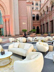Luxurious outdoor seating area with white sofas and gold tables in front of a grand building.