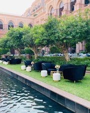 Outdoor seating area with black chairs and tables by a poolside in a luxurious setting.