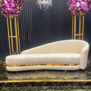 Beige Velvet and gold sofa with decorative flowers and a chandelier in the background