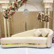 A nice decorative setup with a beige velvet sofa, floral arches, and chandelier in an elegant room.
