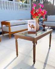 Wooden coffee table with a vase of flowers and a book on a patio setting.