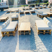 Outdoor seating arrangement made from wooden pallets with white cushions on a stone pavement.