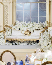 Decorative Gold couch with gold accents surrounded by white flowers in a luxurious setting.