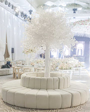 Decorative indoor setting with white floral arrangements and a round beige ottoman.