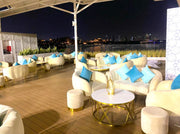 Outdoor evening setting with white furniture, blue pillows, and a cityscape view.