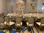 Elegant dining room with a large round table set for a formal dinner, featuring floral centerpieces and gold chairs.