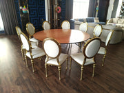 Dining room with a round wooden table and white chairs with gold accents.