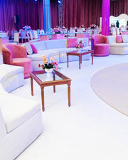 Decorated event space with pink and white furniture, floral arrangements, and purple curtains.