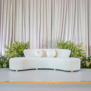 Modern beige sofa with decorative pillows in a minimalistic setting with plants and curtains.