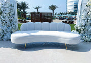 White curved sofa with gold legs in a decorated outdoor setting with flowers and palm trees.