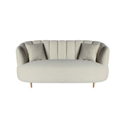 A modern curved loveseat sofa upholstered in a beige velvet fabric, featuring vertical channel tufting on the backrest, two matching throw pillows, and slim gold-toned legs.