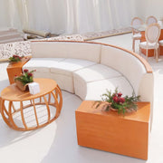 Modern outdoor furniture set with a curved white sofa, wooden coffee table, and decorative plants.