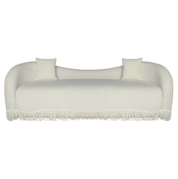 A beige velvet loveseat sofa with a beige fringe trim along the bottom front.