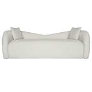 A modern curved beige velvet sofa with two matching square throw pillows, shown from a front-facing perspective