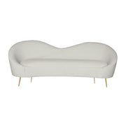 A modern curved chaise lounge chair upholstered in beige velvet with slim gold metal legs.