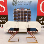 White sofa with two black tables in front of a promotional backdrop for 'Coventry Gardens III'.
