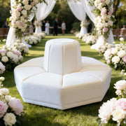 A white modular outdoor seating sofa with a central pedestal backrest, placed on a green lawn under white draped arches and surrounded by pink and white floral arrangements.