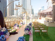Decorative setup with floral arrangements and chairs on a rooftop with city skyline in the background