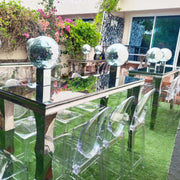 Clear glass chairs and table set outdoors with decorative lights.