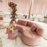 Pink curved sofa in a stylish room with floral decorations and tables.