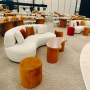 Modern interior with white curved sofa, orange stools, and wooden tables.