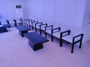 Modern office waiting area with white chairs and black tables against a light purple wall.